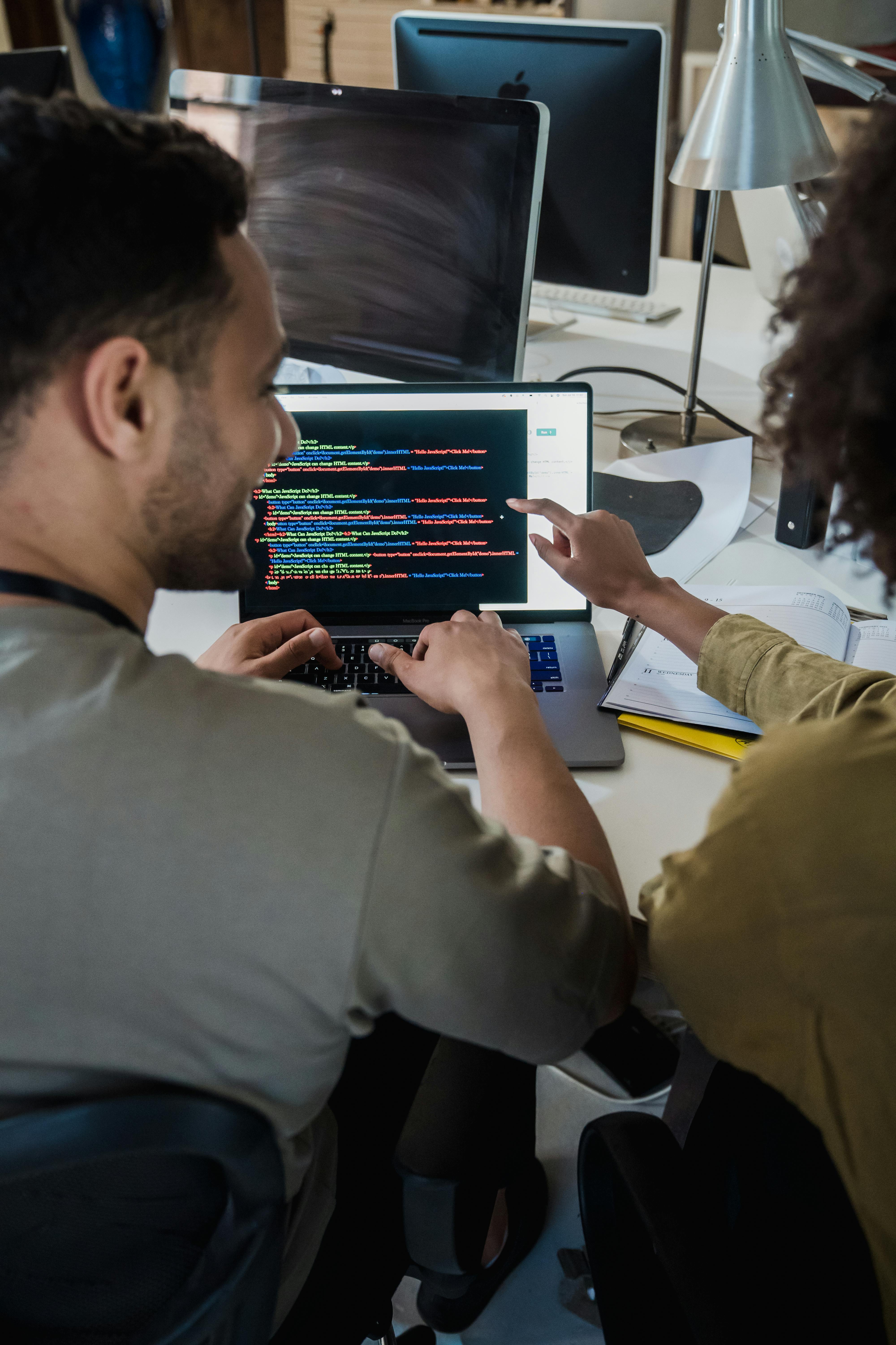 Two programmers working together on a laptop, discussing code in a modern office setting.